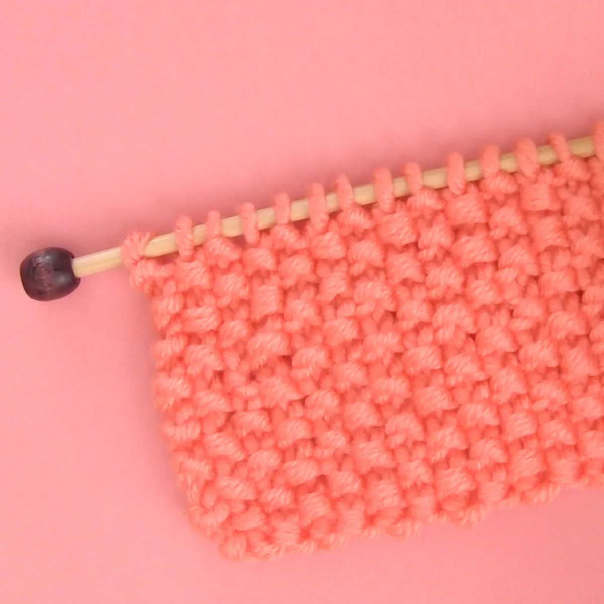 Seed Stitch Knitting swatch on a knitting needle in orange yarn.