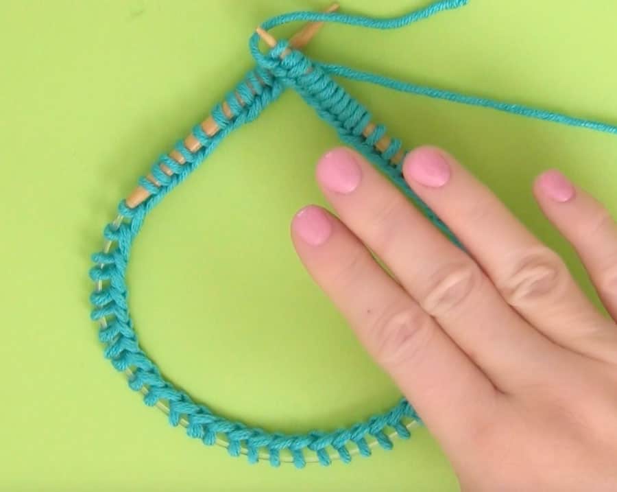 Cast on stitches onto a circular knitting needle in blue yarn on a green background with woman's hand