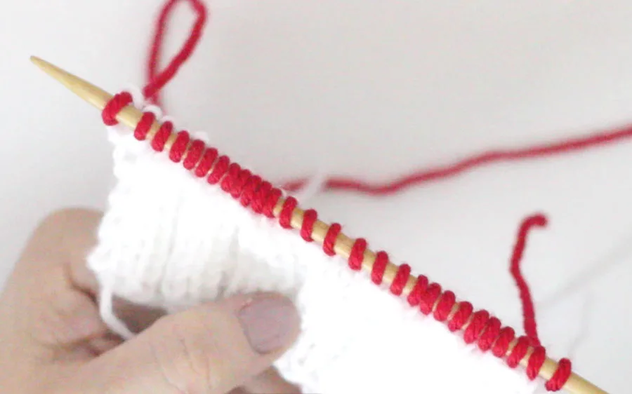 Red yarn change on knitting needle with white rib stitch pattern beneath it.