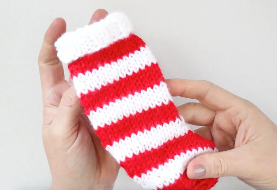 Finished knitted mini stocking in red and white stripes being held by woman's hands