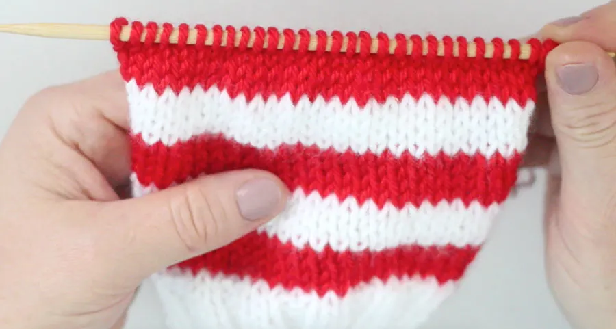 Red and White stripe knitting piece on a knitting needle in the Stockinette Stitch
