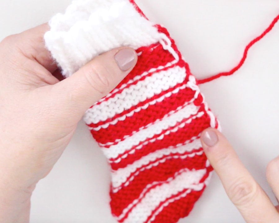 Wrong side out of knitted mini stocking to tack sides together with yarn and tapestry needle