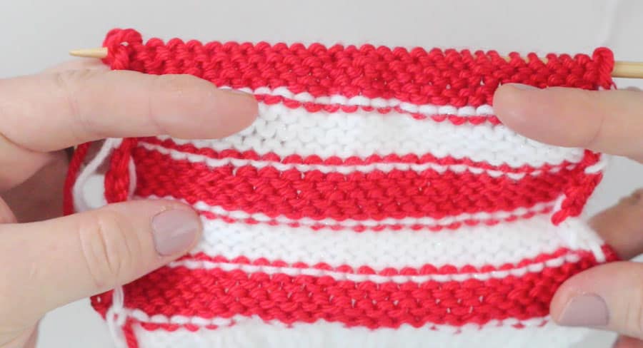 Wrong side of the work for the mini stocking in red and white yarn being held by hands