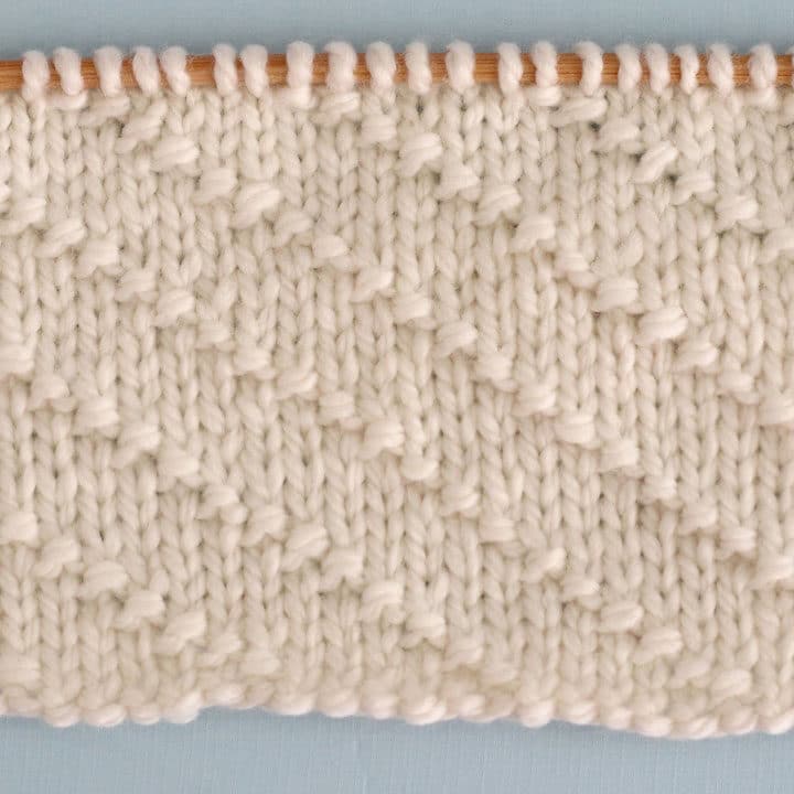 Swatch of textured Diagonal Seed Stitch swatch in white yarn on a knitting needle