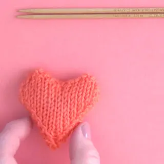 Knit Heart in orange yarn color with hand and knitting needles