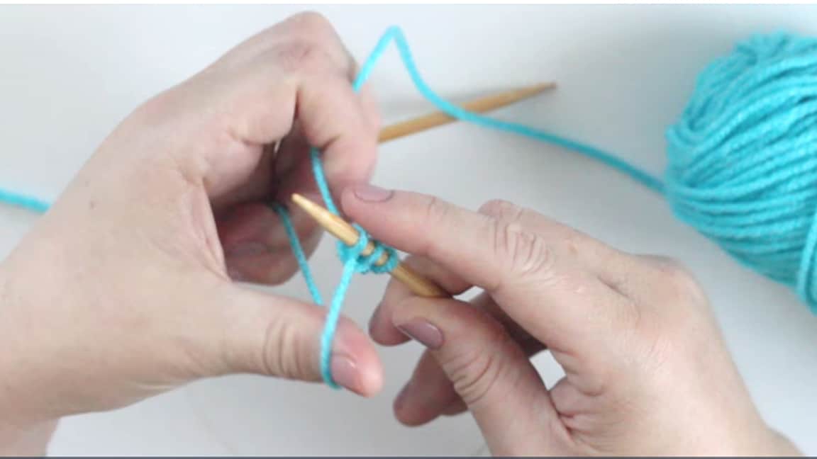 Hands casting on knitting stitches in blue yarn onto a circular knitting needle.