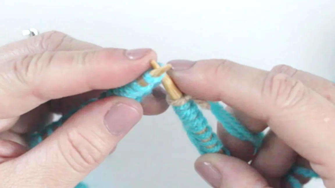 Weaving in yarn tail demonstration on circular knitting needles with hands.