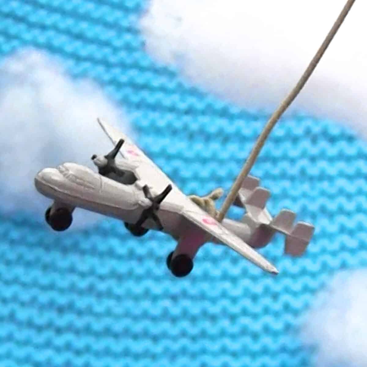 Toy airplane over swatch of knitted garter stitch blanket in blue yarn color with poly-fill clouds.