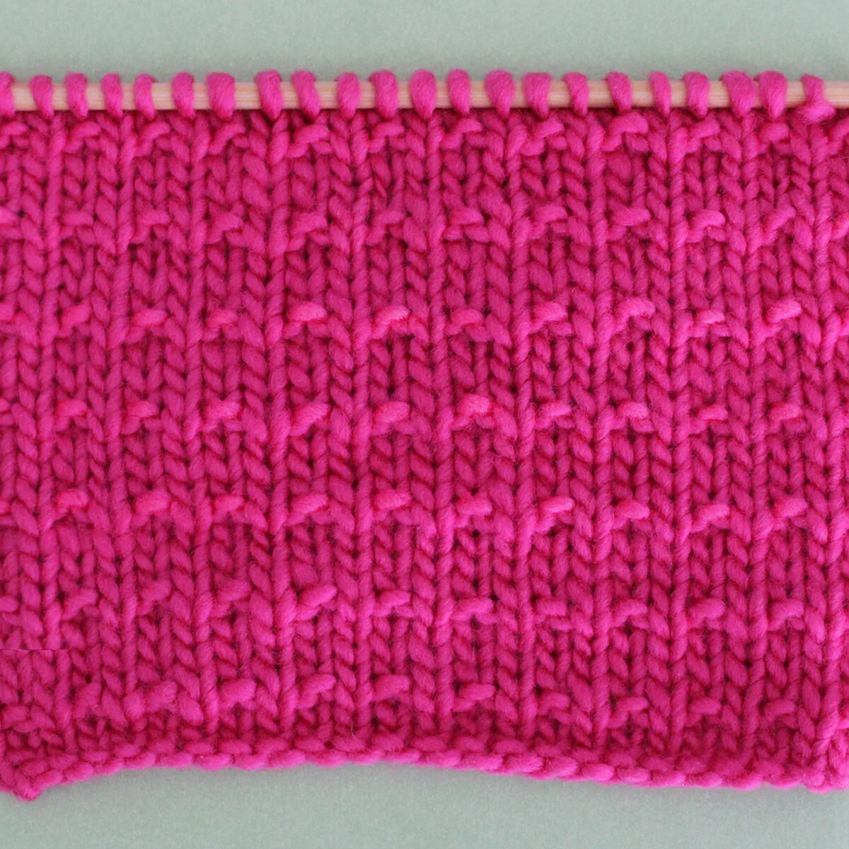 Andalusian Knit Stitch Pattern texture in pink color yarn on knitting needle.