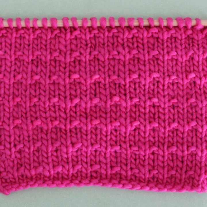 Andalusian Knit Stitch Pattern texture in pink color yarn on knitting needle.