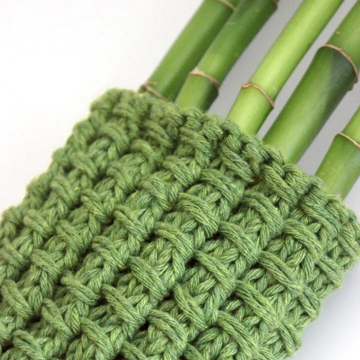 Knitted Bamboo Stitch Pattern swatch in green color yarn wrapped around bamboo stalks.