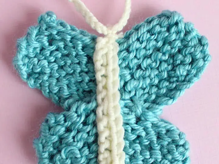Knitted butterfly shape in blue color yarn atop a pink background.