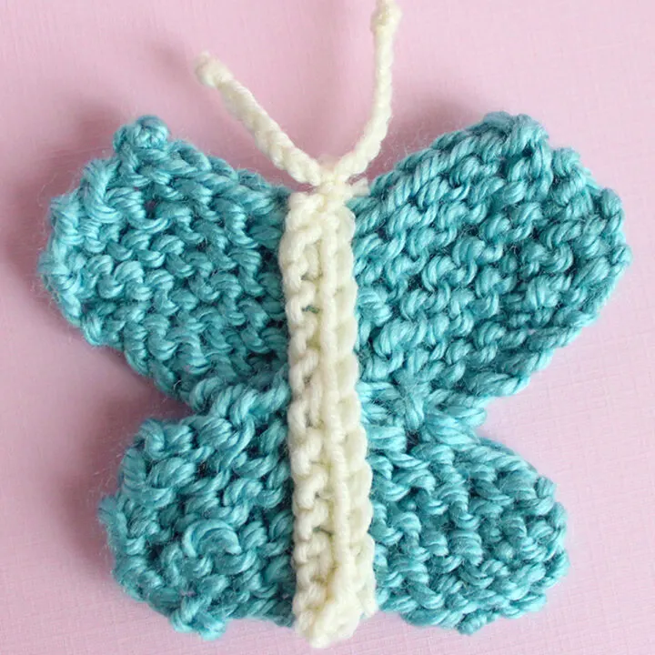 Knitted butterfly shape in blue color yarn atop a pink background.