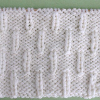 Caterpillar Knit Stitch Pattern in white yarn on knitting needle.