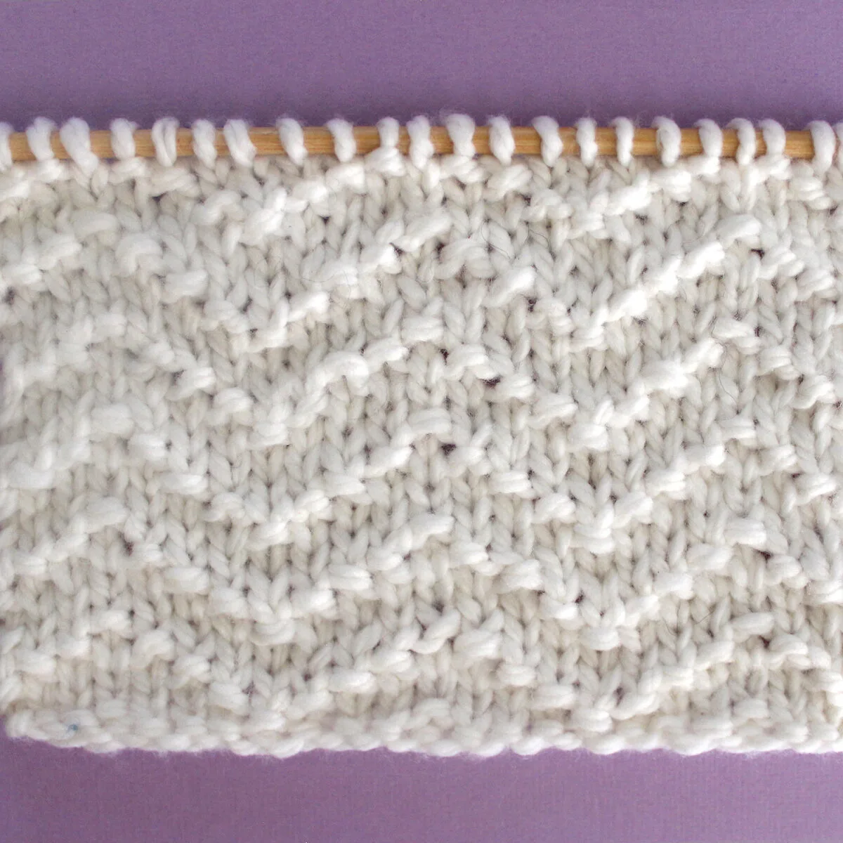 Chevron Seed Knit Stitch Pattern texture in white color yarn on knitting needle.