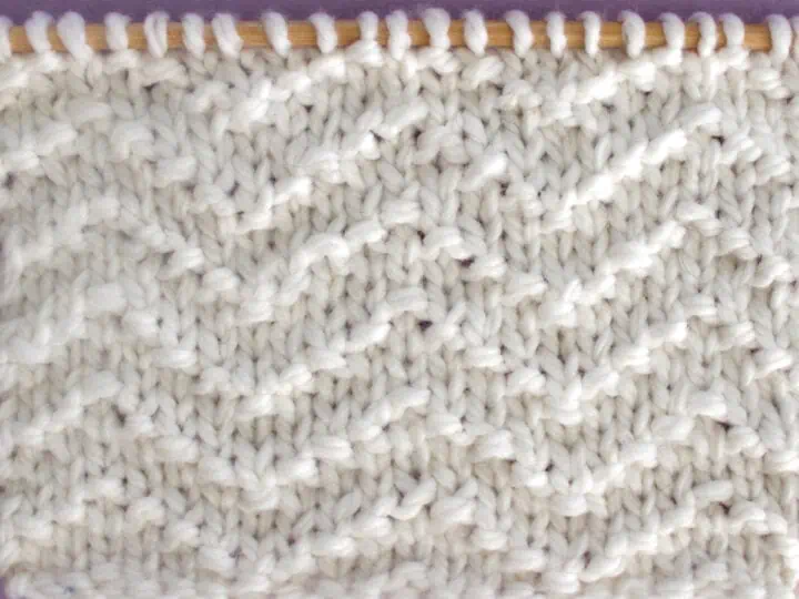 Chevron Seed Knit Stitch Pattern texture in white color yarn on knitting needle.