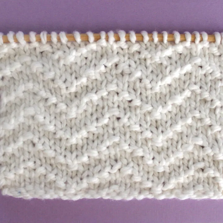 Chevron Seed Knit Stitch Pattern texture in white color yarn on knitting needle.