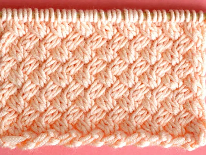 Diagonal Basket Weave Cable Knit Stitch Pattern texture in peach color yarn on knitting needle.