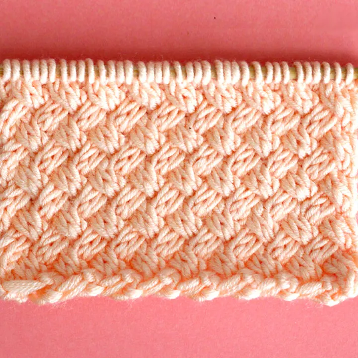 Diagonal Basket Weave Cable Knit Stitch Pattern texture in peach color yarn on knitting needle.