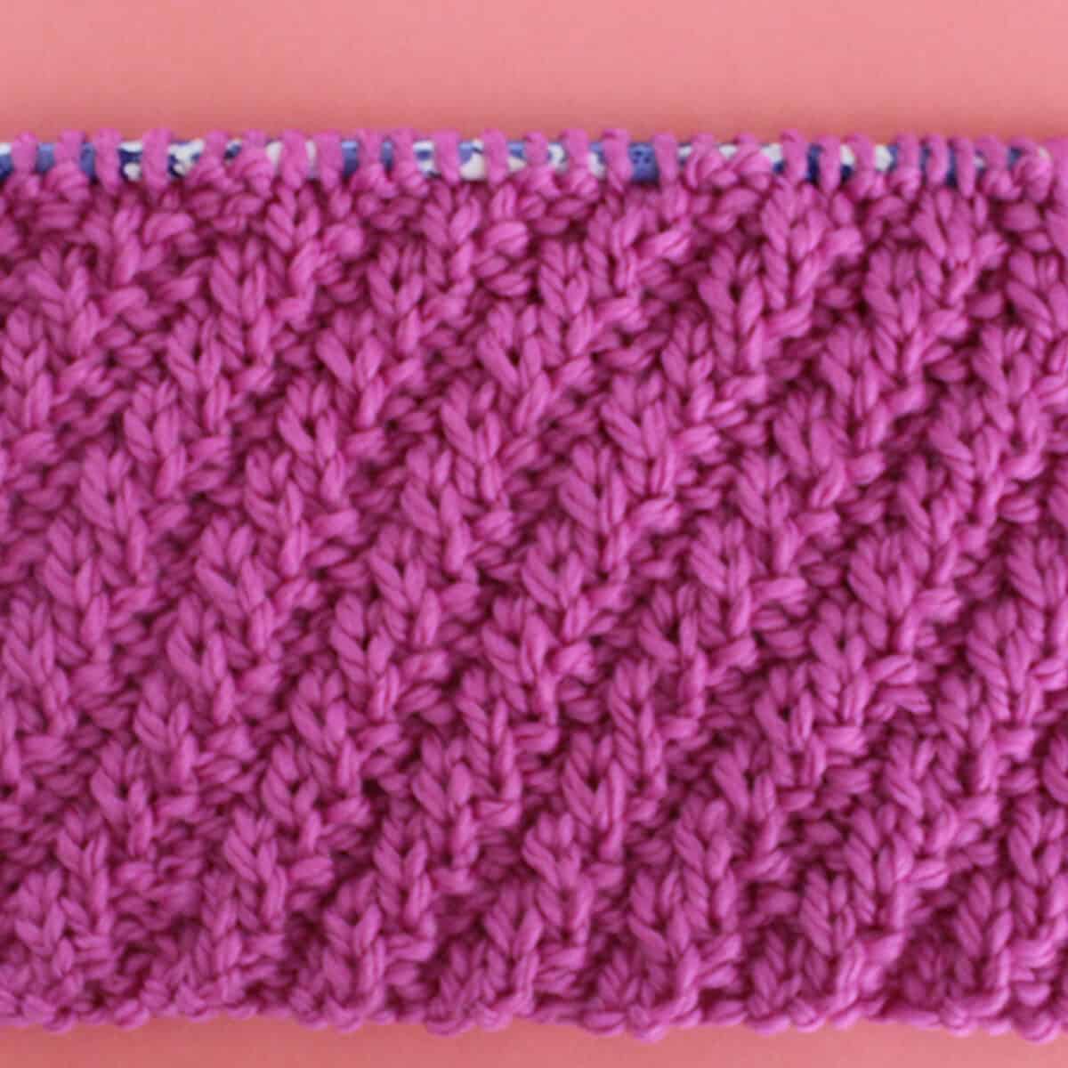 Diagonal Rib Cable Knit Stitch Pattern texture in pink color yarn on knitting needle.