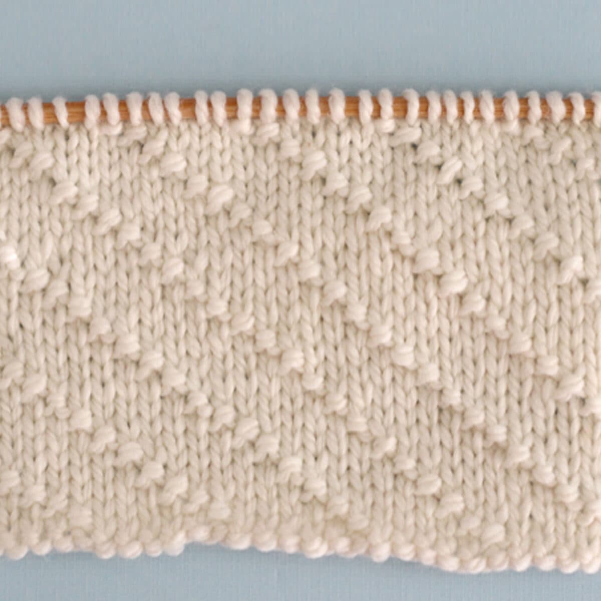 Diagonal Seed Knit Stitch Pattern in white yarn on knitting needle.