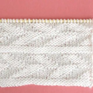 Knitted Embossed Leaf Stitch Pattern in white yarn on knitting needle.