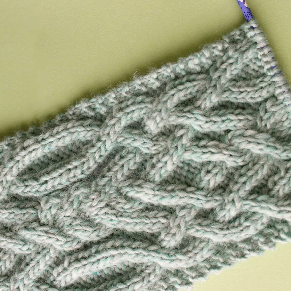 Knitted Fancy Celtic Cable Stitch Scarf in Green yarn color on a knitting needle.