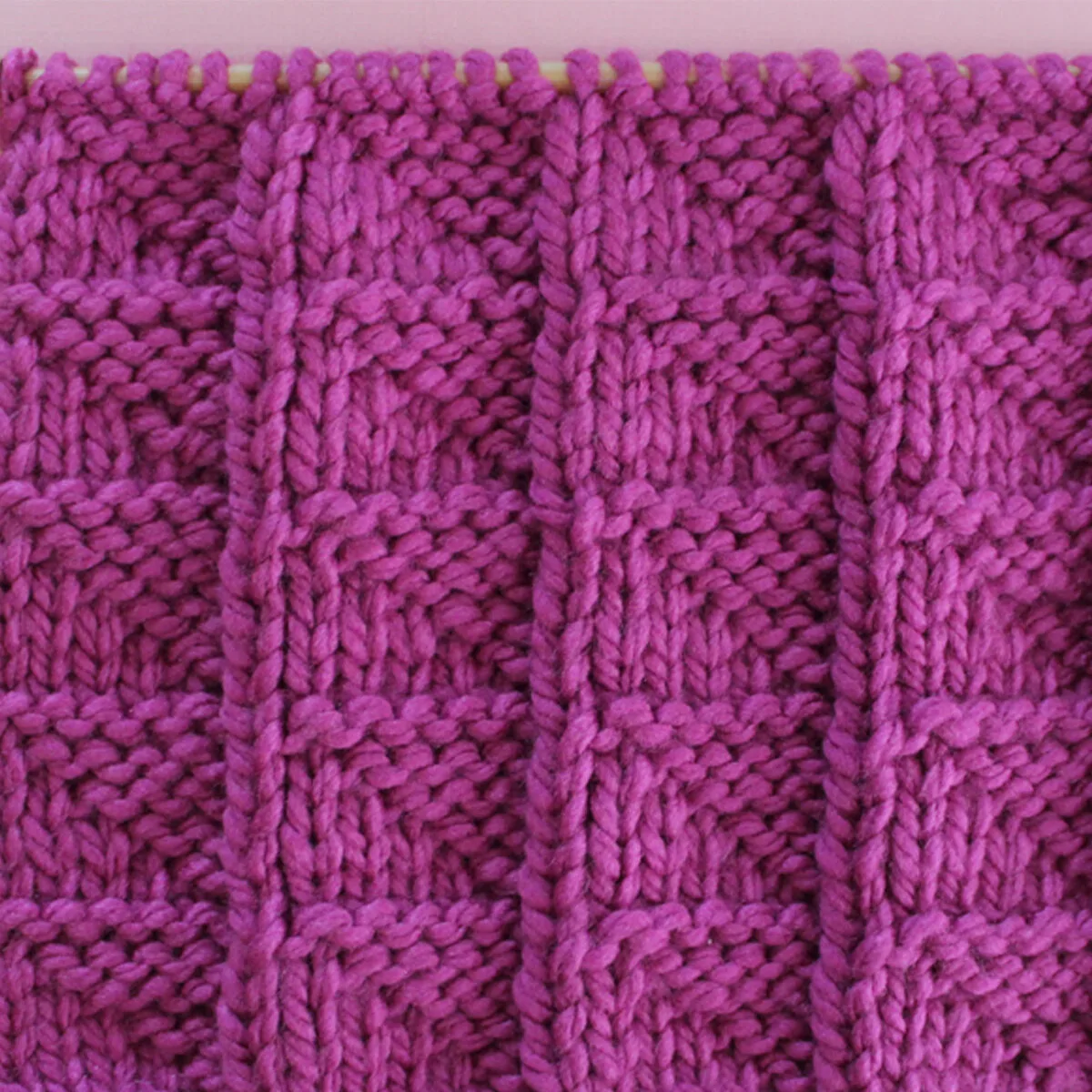 Knitted Flag Stitch Pattern in purple yarn on knitting needle.