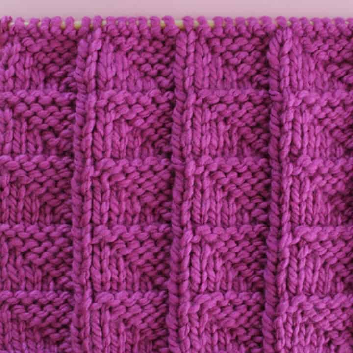 Knitted Flag Stitch Pattern in purple yarn on knitting needle.
