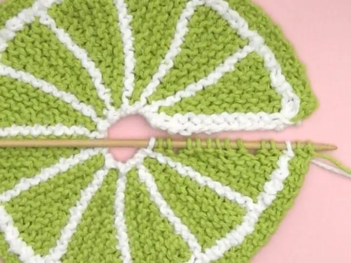 Knitted fruit slice shape in green color yarn atop a pink background.