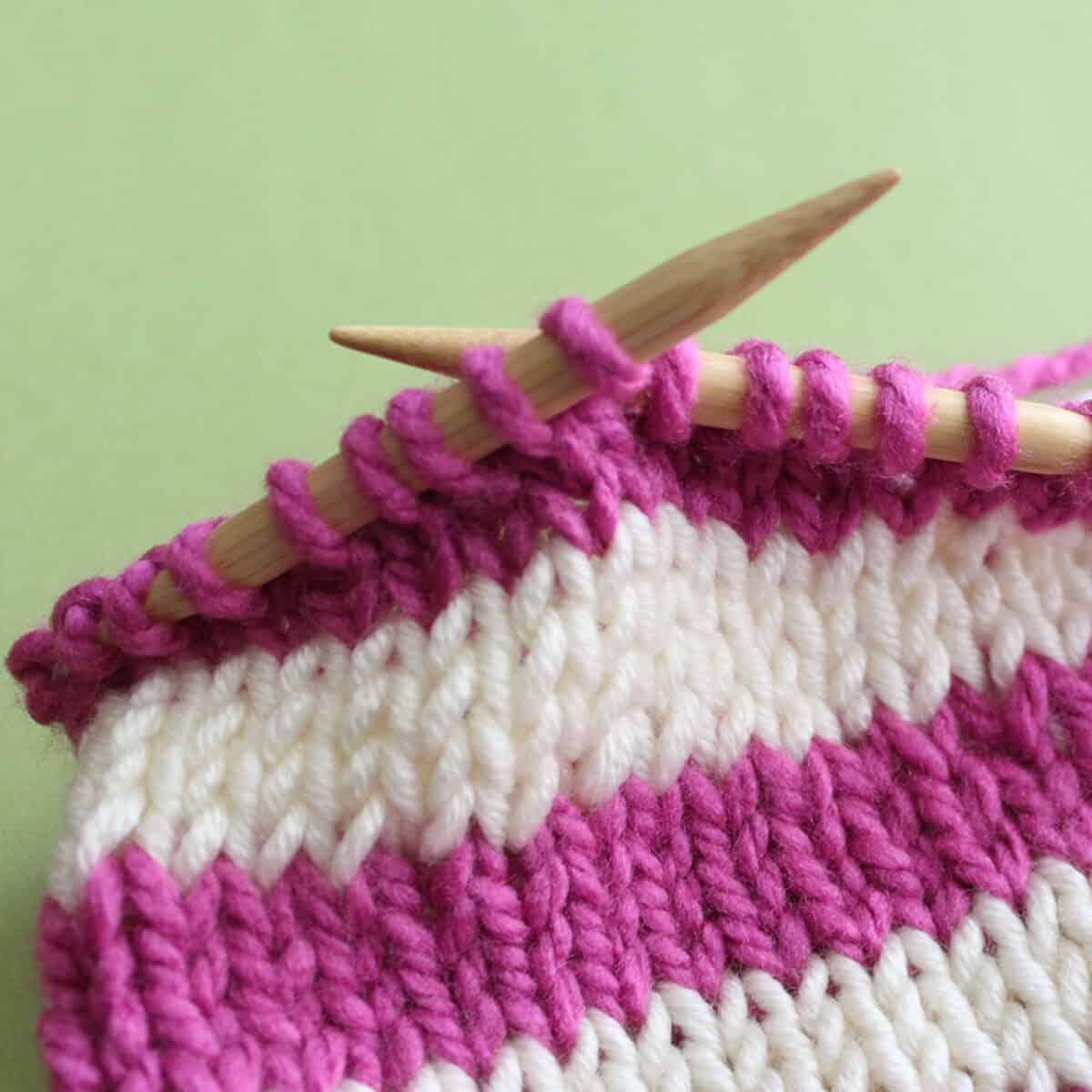 Knitted sample in horizontal stripes in pink and white yarn color on circular knitting needles.
