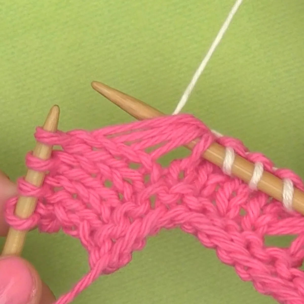 Pink yarn on knitting needle with white color yarn demonstrating Knit Below technique.