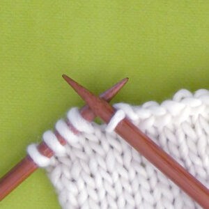Knitted swatch of white yarn in stockinette stitch pattern with two wooden knitting needles.