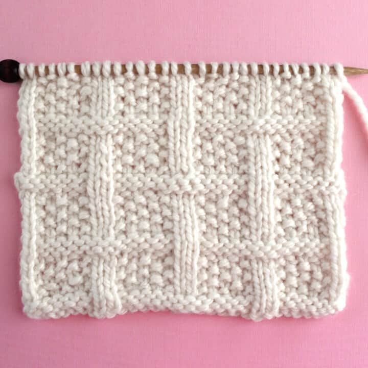 Lattice Seed Knit Stitch Pattern texture in white color yarn on knitting needle atop a pink background.