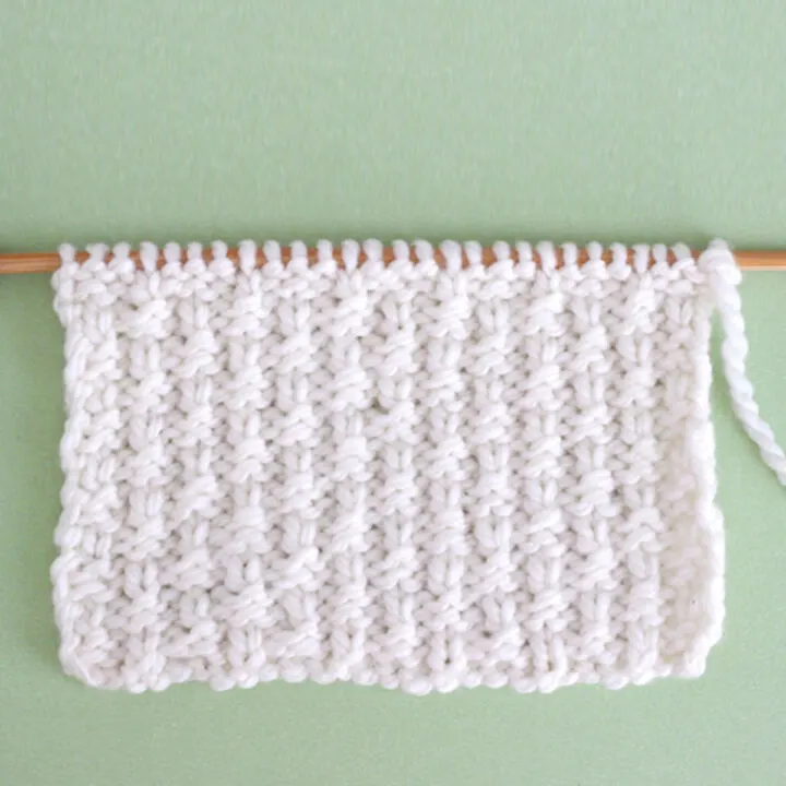 Little Raindrops Knit Stitch Pattern in white yarn on knitting needle atop a green background.