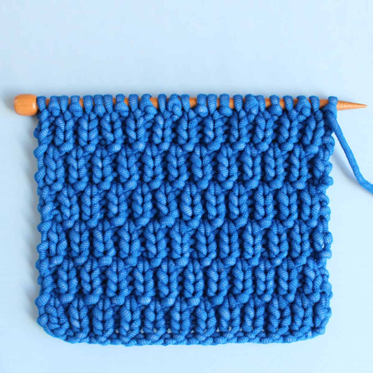 Long Raindrops Knit Stitch Pattern in bright blue yarn color on knitting needle atop a light blue background.