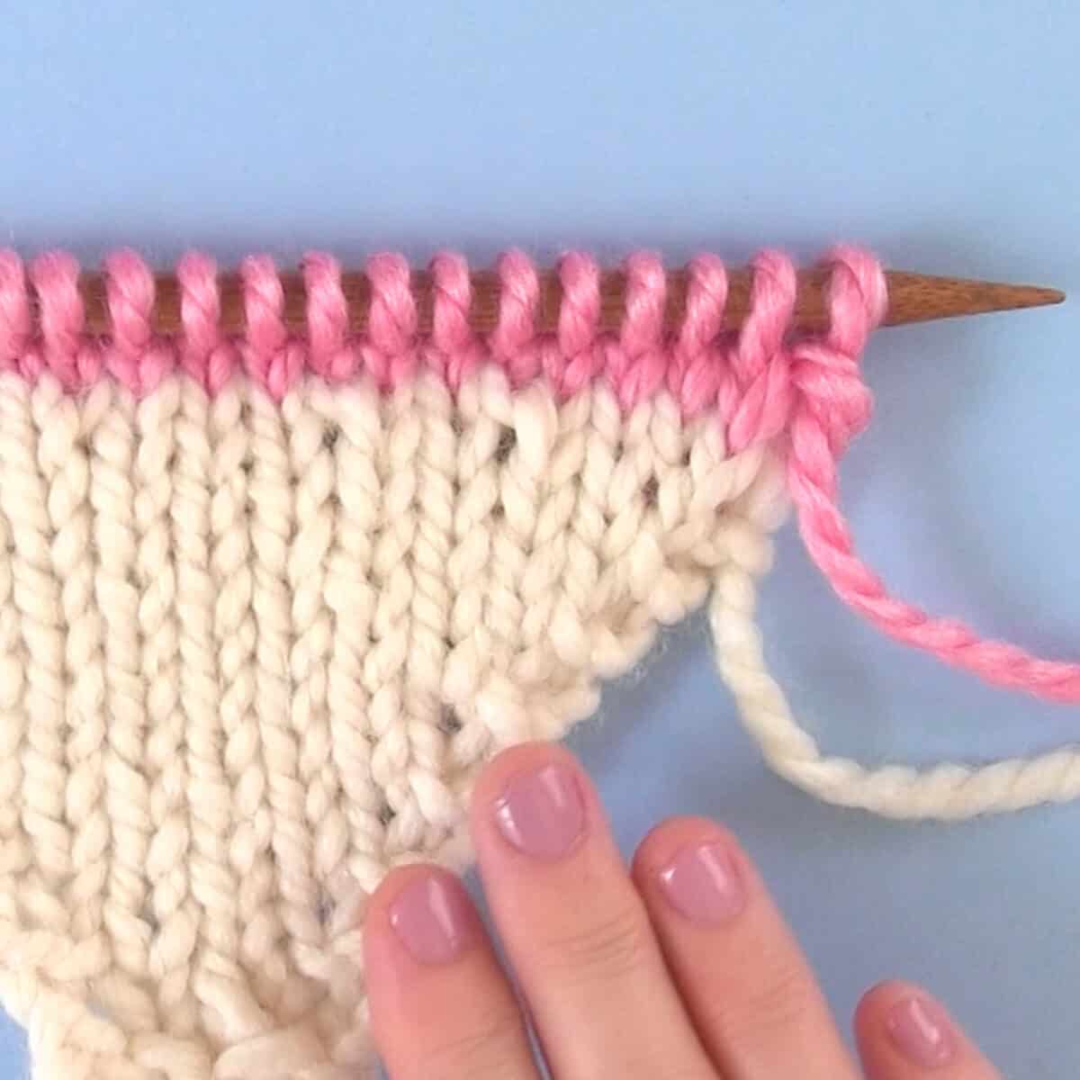 Make One Knitting Increase Sample in white and pink yarn with woman's hand