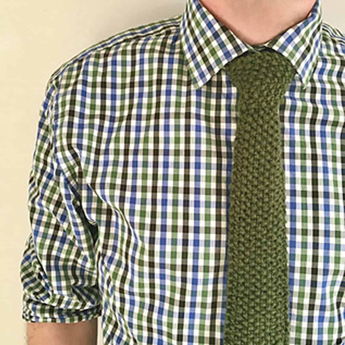 Knitted Necktie in seed stitch pattern with green yarn worn by a model in a checkered shirt.