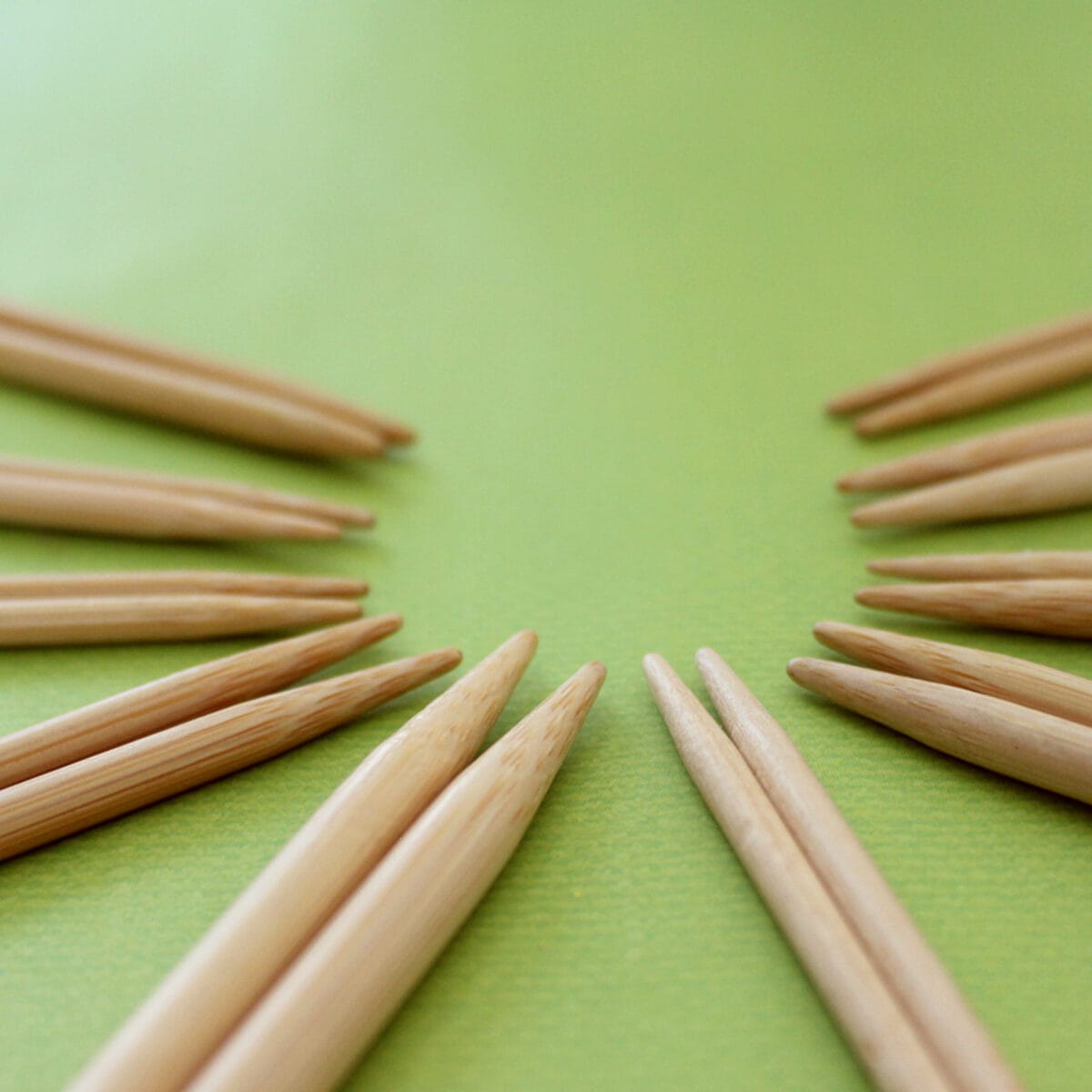Ten pairs of wooden bamboo knitting needles arranged in a circular pattern atop a green background.