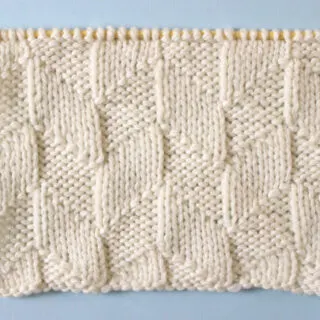 Parallelogram Knit Stitch Pattern texture in white yarn on knitting needle.