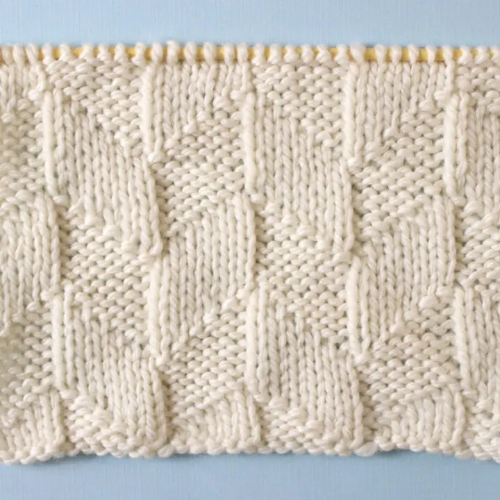 Parallelogram Knit Stitch Pattern texture in white yarn on knitting needle.