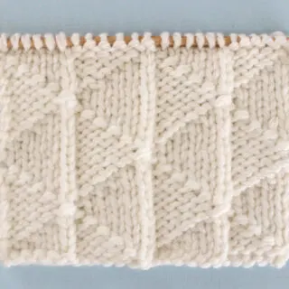 Pennant Pleating Knit Stitch Pattern in white yarn on knitting needle.