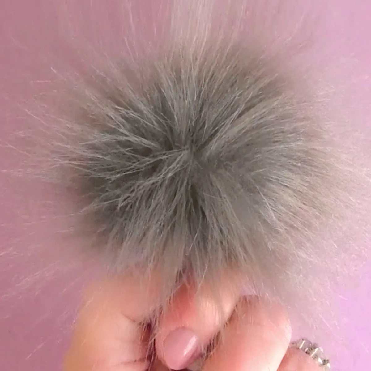 Pom Pom in Faux Fur Fabric in color grey held by hand.