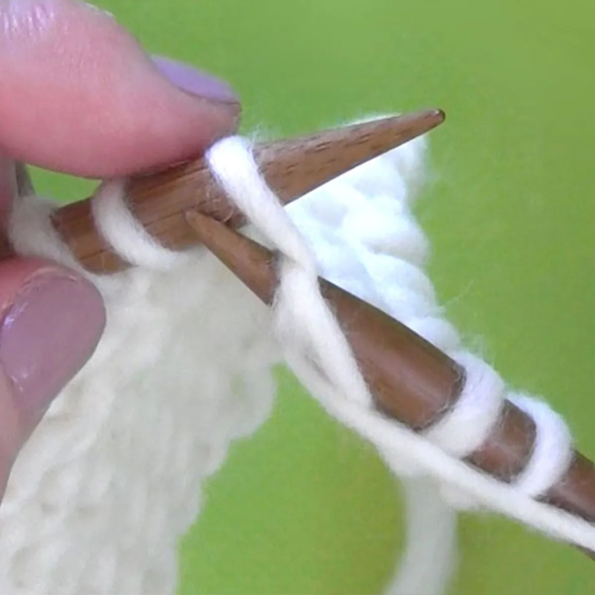 Hands purl stitch with knitting needle and white color yarn.