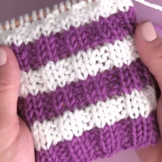 Knitted horizontal stripe pattern in rib stitch texture with purple and white yarn colors held by hands.