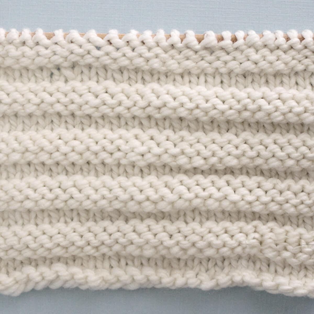 Knitted Reverse Ridge Stitch Pattern in white yarn on knitting needle.