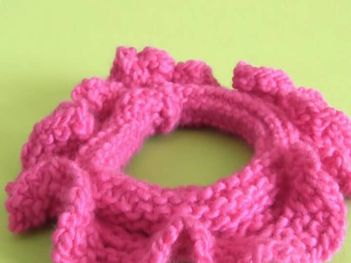 Knitted Hair Scrunchie in hot pink yarn color laying on a green background.