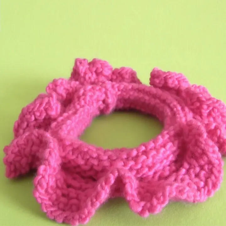 Knitted Hair Scrunchie in hot pink yarn color laying on a green background.