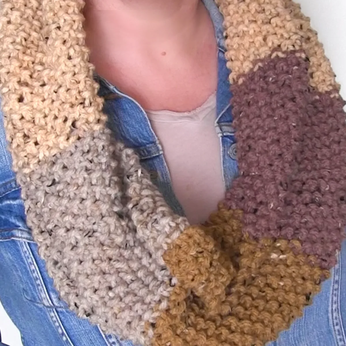 Knitted Seed Stitch Infinity Scarf in different shades of brown yarn colors worn by woman in jean jacket.