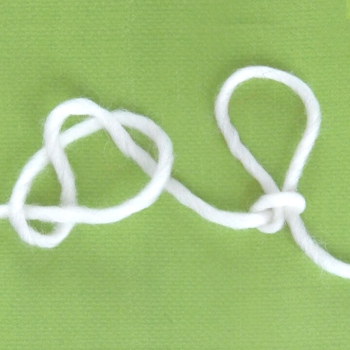 White yarn demonstrating the Slip Knot technique atop a green background.